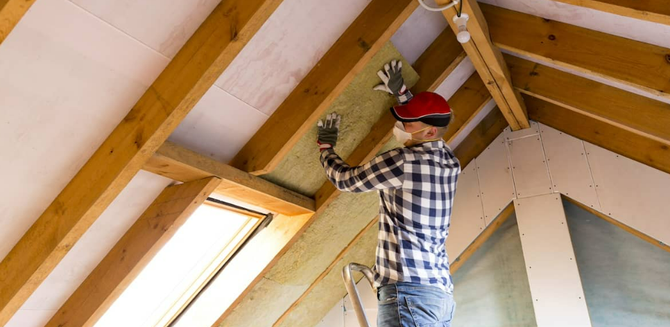 A man installs attic insulation for energy efficiency and comfort.